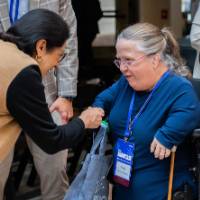 A woman shaking the hand of another woman in a motorized wheelchair